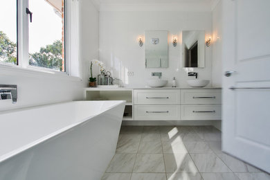 シドニーにある高級な広い北欧スタイルのおしゃれなマスターバスルーム (シェーカースタイル扉のキャビネット、白いキャビネット、置き型浴槽、コーナー設置型シャワー、壁掛け式トイレ、白いタイル、磁器タイル、白い壁、大理石の床、コンソール型シンク、クオーツストーンの洗面台、白い床、オープンシャワー) の写真