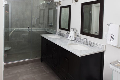 This is an example of a medium sized traditional ensuite bathroom in Tampa with flat-panel cabinets, black cabinets, an alcove shower, a two-piece toilet, white walls, ceramic flooring, a submerged sink, marble worktops, grey floors and a hinged door.
