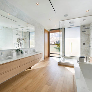 Ejemplo de cuarto de baño principal, contemporáneo, grande, con armarios con paneles lisos, puertas de armario de madera clara, bañera exenta, ducha doble, baldosas y/o azulejos blancos, losas de piedra, paredes blancas, suelo de madera clara, lavabo bajoencimera, ducha con puerta con bisagras, encimeras blancas, sanitario de una pieza, encimera de mármol y suelo beige