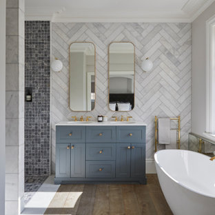 Photo of a classic ensuite bathroom in Essex with shaker cabinets, blue cabinets, a freestanding bath, a built-in shower, white walls, a submerged sink, brown floors, an open shower and white worktops.