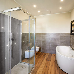 Idee per una stanza da bagno padronale minimal con doccia a filo pavimento, piastrelle grigie, porta doccia scorrevole, vasca ad angolo, bidè, pavimento in legno massello medio, pavimento marrone e pareti grigie