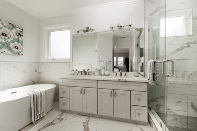 Modelo de cuarto de baño tradicional renovado con armarios estilo shaker, puertas de armario grises, bañera exenta, paredes blancas, lavabo bajoencimera, suelo gris y encimeras blancas