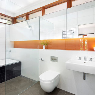Foto på ett mellanstort funkis en-suite badrum, med ett väggmonterat handfat, ett platsbyggt badkar, en kantlös dusch, en vägghängd toalettstol, svart kakel, keramikplattor, vita väggar, klinkergolv i keramik och grått golv