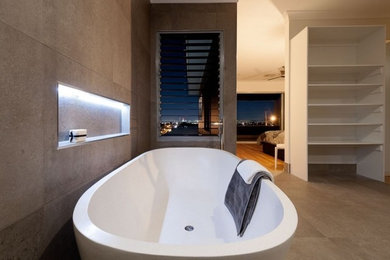 Cette image montre une salle de bain principale design de taille moyenne avec un placard à porte plane, des portes de placard blanches, une baignoire indépendante, un carrelage gris, des carreaux de béton, un mur gris, carreaux de ciment au sol, une vasque et un sol gris.