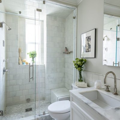Alcove shower - mid-sized traditional master white tile and subway tile marble floor and gray floor alcove shower idea in New York with recessed-panel cabinets, white cabinets, a two-piece toilet, beige walls, an undermount sink, marble countertops, a hinged shower door and white countertops