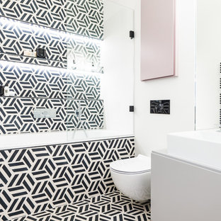 Inspiration for a medium sized eclectic bathroom in London with flat-panel cabinets, white cabinets, an alcove bath, a shower/bath combination, a wall mounted toilet, black and white tiles, white walls, a vessel sink, multi-coloured floors and white worktops.
