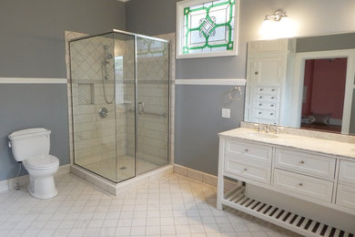 На фото: ванная комната в классическом стиле с фасадами в стиле шейкер, белыми фасадами, угловым душем, белой плиткой, керамогранитной плиткой, серыми стенами, полом из керамогранита, врезной раковиной и мраморной столешницей