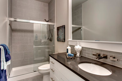 На фото: ванная комната среднего размера в стиле неоклассика (современная классика) с открытыми фасадами, белыми фасадами, ванной в нише, душем в нише, унитазом-моноблоком, серой плиткой, стеклянной плиткой, серыми стенами, полом из ламината, душевой кабиной, монолитной раковиной и столешницей из известняка с