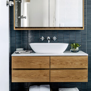 Photo of a contemporary bathroom in Sydney with flat-panel cabinets, medium wood cabinets, blue tile, mosaic tile, blue walls, a vessel sink, grey floor and white benchtops.