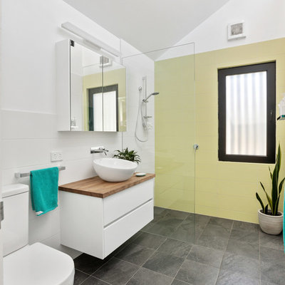 Inspiration for a contemporary 3/4 yellow tile gray floor bathroom remodel in Perth with flat-panel cabinets, white cabinets, a two-piece toilet, white walls, a vessel sink, wood countertops and brown countertops