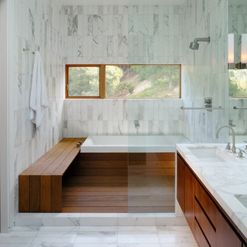 White marble bathroom with window for light and wood bench in the shower