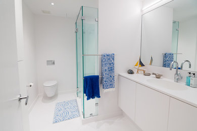 Example of a mid-sized minimalist master white tile white floor corner shower design in Philadelphia with flat-panel cabinets, white cabinets, a wall-mount toilet, white walls, an integrated sink, solid surface countertops, a hinged shower door and white countertops