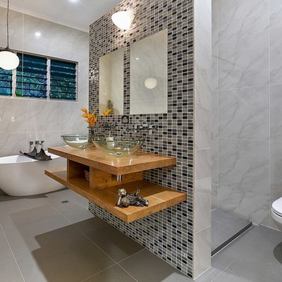 Freestanding bathtub - mid-sized contemporary master gray tile and multicolored tile gray floor freestanding bathtub idea in Cairns with open cabinets, light wood cabinets, a two-piece toilet, gray walls, a vessel sink and wood countertops