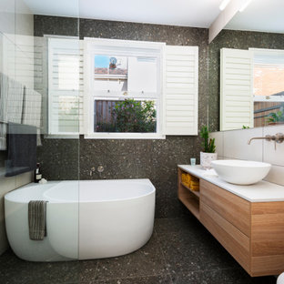 Photo of a mid-sized contemporary master bathroom in Melbourne with furniture-like cabinets, medium wood cabinets, a freestanding tub, an open shower, a wall-mount toilet, pink tile, ceramic tile, multi-coloured walls, ceramic floors, a vessel sink, granite benchtops, grey floor, an open shower, white benchtops, a single vanity and a floating vanity.