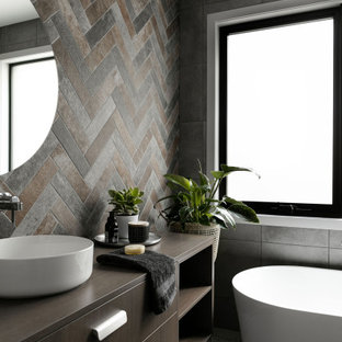Mid-sized contemporary master bathroom in Melbourne with flat-panel cabinets, medium wood cabinets, a freestanding tub, brown tile, gray tile, a vessel sink, wood benchtops, grey floor, brown benchtops, a single vanity and a freestanding vanity.