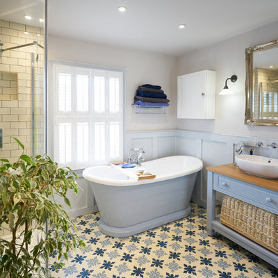Bathroom - large coastal master beige tile and subway tile mosaic tile floor and blue floor bathroom idea in Sussex with raised-panel cabinets, blue cabinets, gray walls, wood countertops, a hinged shower door, a vessel sink and brown countertops