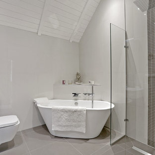This is an example of a contemporary ensuite bathroom in Hertfordshire with a freestanding bath, a corner shower, grey tiles, grey walls, an integrated sink, grey floors and a hinged door.