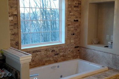 Example of a mid-sized classic master brown tile and stone tile travertine floor and brown floor drop-in bathtub design in Milwaukee with recessed-panel cabinets, distressed cabinets, beige walls, granite countertops and black countertops