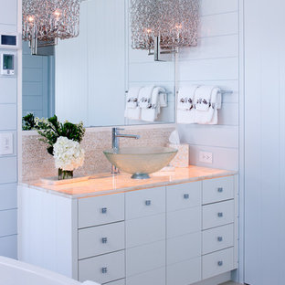 Photo of a small beach style master bathroom in Boston with a vessel sink, flat-panel cabinets, white cabinets, onyx benchtops, a freestanding tub, blue walls and travertine floors.