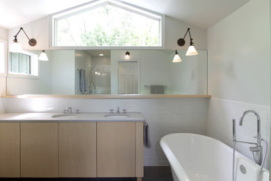 Modelo de cuarto de baño moderno con armarios con paneles lisos, puertas de armario de madera clara, bañera exenta, ducha empotrada y lavabo bajoencimera