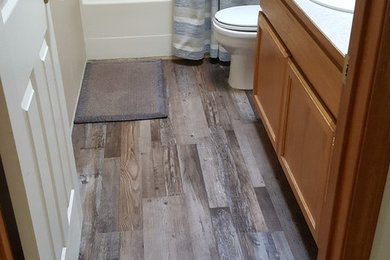 Transitional medium tone wood floor and brown floor bathroom photo in Seattle with recessed-panel cabinets, light wood cabinets, a two-piece toilet, a drop-in sink and gray countertops