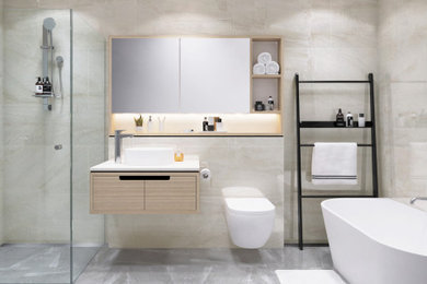 Modelo de cuarto de baño principal moderno con puertas de armario beige, bañera exenta, ducha esquinera, sanitario de pared, encimera de mármol, ducha con puerta con bisagras y encimeras blancas