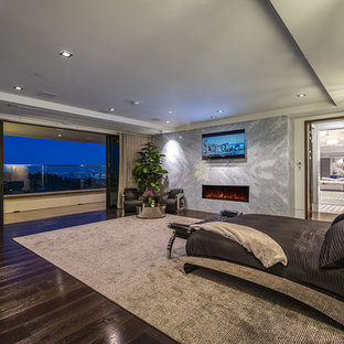 Großes Modernes Gästezimmer mit grauer Wandfarbe, dunklem Holzboden, Hängekamin, Kaminumrandung aus Stein, braunem Boden und eingelassener Decke in Los Angeles