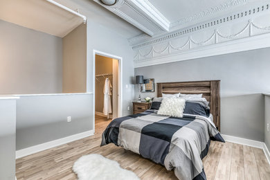 Diseño de dormitorio principal moderno pequeño sin chimenea con paredes grises, suelo de madera clara y suelo marrón