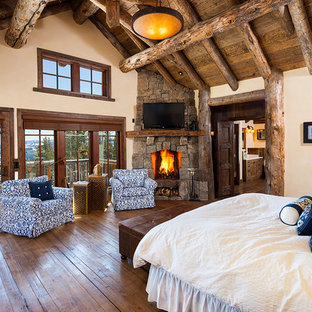 Foto de dormitorio principal, rústico, grande, con paredes beige, suelo de madera oscura, chimenea de esquina y marco de chimenea de piedra