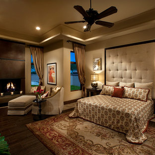Réalisation d'une grand chambre parentale méditerranéenne avec un mur beige, un sol en bois foncé, une cheminée standard et un manteau de cheminée en bois.