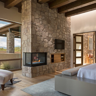 Foto de dormitorio principal, de estilo americano, grande, con paredes beige, chimenea de esquina, marco de chimenea de piedra, suelo marrón y suelo de madera clara