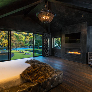 Diseño de dormitorio principal, actual, con paredes negras, suelo de madera oscura, chimenea lineal, marco de chimenea de hormigón y suelo marrón