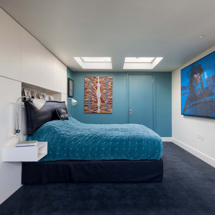 Immagine di una grande camera degli ospiti moderna con pareti blu, moquette, camino lineare Ribbon, cornice del camino in intonaco e pavimento nero