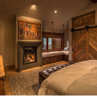 Ejemplo de dormitorio principal, rural, de tamaño medio, con paredes grises, suelo de madera clara, chimenea tradicional y marco de chimenea de hormigón