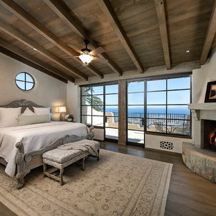 Ejemplo de dormitorio principal, mediterráneo, de tamaño medio, con paredes beige, suelo de madera oscura, chimenea de esquina, marco de chimenea de piedra y suelo marrón