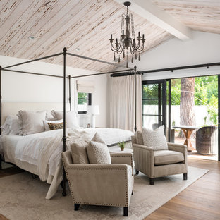 Modelo de dormitorio principal, campestre, grande, con paredes blancas, suelo de madera en tonos medios y suelo marrón