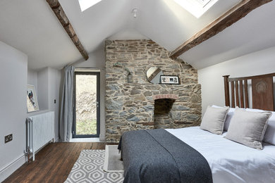 Photo of a medium sized scandinavian guest bedroom with white walls, dark hardwood flooring, a standard fireplace, a stone fireplace surround, brown floors and exposed beams.