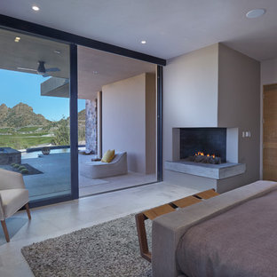 Foto de dormitorio principal, de estilo americano, grande, con paredes beige, suelo de baldosas de porcelana, chimenea de esquina, marco de chimenea de hormigón y suelo gris