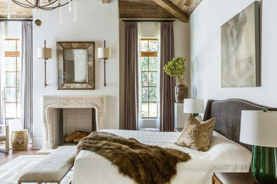 Großes Country Hauptschlafzimmer mit weißer Wandfarbe, hellem Holzboden, Kamin, gefliester Kaminumrandung und beigem Boden in Houston
