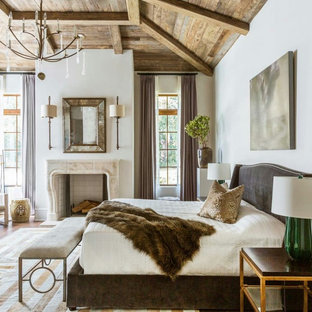 Großes Country Hauptschlafzimmer mit weißer Wandfarbe, hellem Holzboden, Kamin, gefliester Kaminumrandung und beigem Boden in Houston