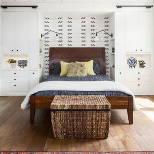 Ejemplo de dormitorio principal, de estilo de casa de campo, extra grande, sin chimenea, con paredes beige, suelo de madera en tonos medios, marco de chimenea de ladrillo y suelo marrón