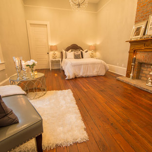 Foto de dormitorio principal, clásico, grande, con paredes beige, suelo de madera oscura, chimenea tradicional y marco de chimenea de ladrillo