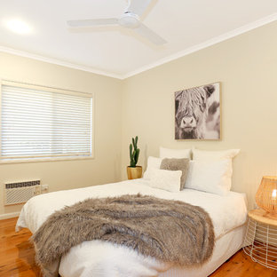 This is an example of a beach style guest bedroom in Brisbane with beige walls, medium hardwood floors and brown floor.