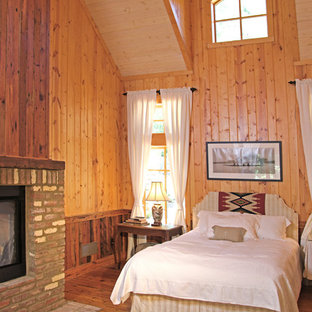 Diseño de dormitorio de estilo de casa de campo, de tamaño medio, con suelo de madera en tonos medios, chimenea de doble cara y marco de chimenea de ladrillo