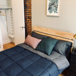 Imagen de habitación de invitados de tamaño medio, sin chimenea, con paredes beige, suelo de madera clara, marco de chimenea de ladrillo y suelo beige