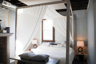 Ejemplo de dormitorio tipo loft moderno de tamaño medio con paredes grises, suelo de madera en tonos medios, estufa de leña, marco de chimenea de ladrillo y suelo gris