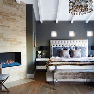 Ejemplo de dormitorio principal, actual, de tamaño medio, con paredes grises, suelo de madera en tonos medios, chimenea lineal y marco de chimenea de baldosas y/o azulejos