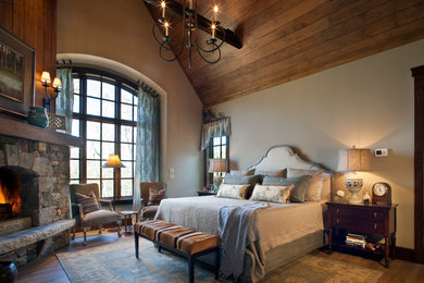 Example of a transitional master dark wood floor bedroom design in Other with beige walls and a stone fireplace