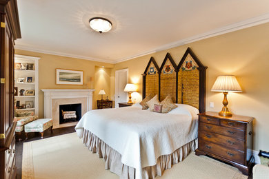 Modelo de dormitorio principal tradicional grande con paredes beige, suelo de madera oscura, todas las chimeneas y marco de chimenea de madera