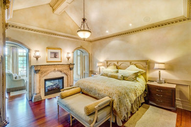 Ejemplo de dormitorio principal clásico grande con paredes beige, suelo de madera en tonos medios, chimenea de doble cara, marco de chimenea de yeso y suelo marrón